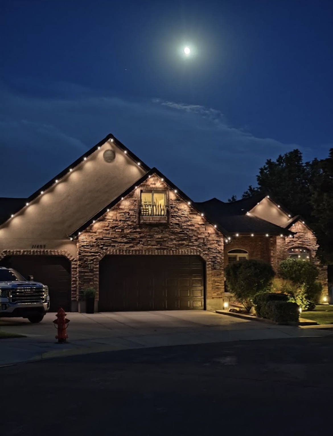 Warm white permanent roofline lights on a stone home at night